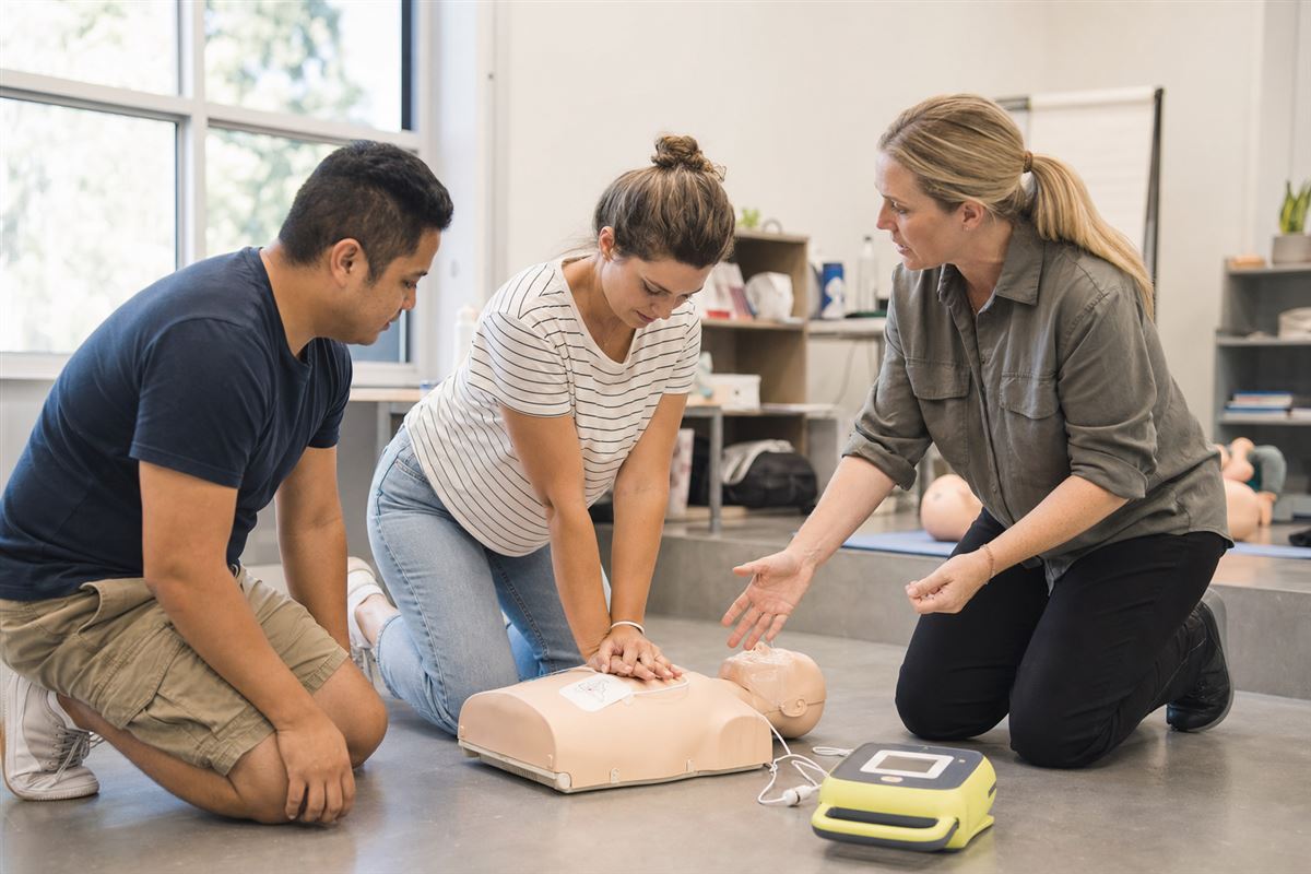 First aid trainer coaching adult learners practising CPR on a manikin