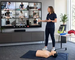 Instructor leading a live Google Meet first aid class with remote learners, an adult manikin and training equipment
